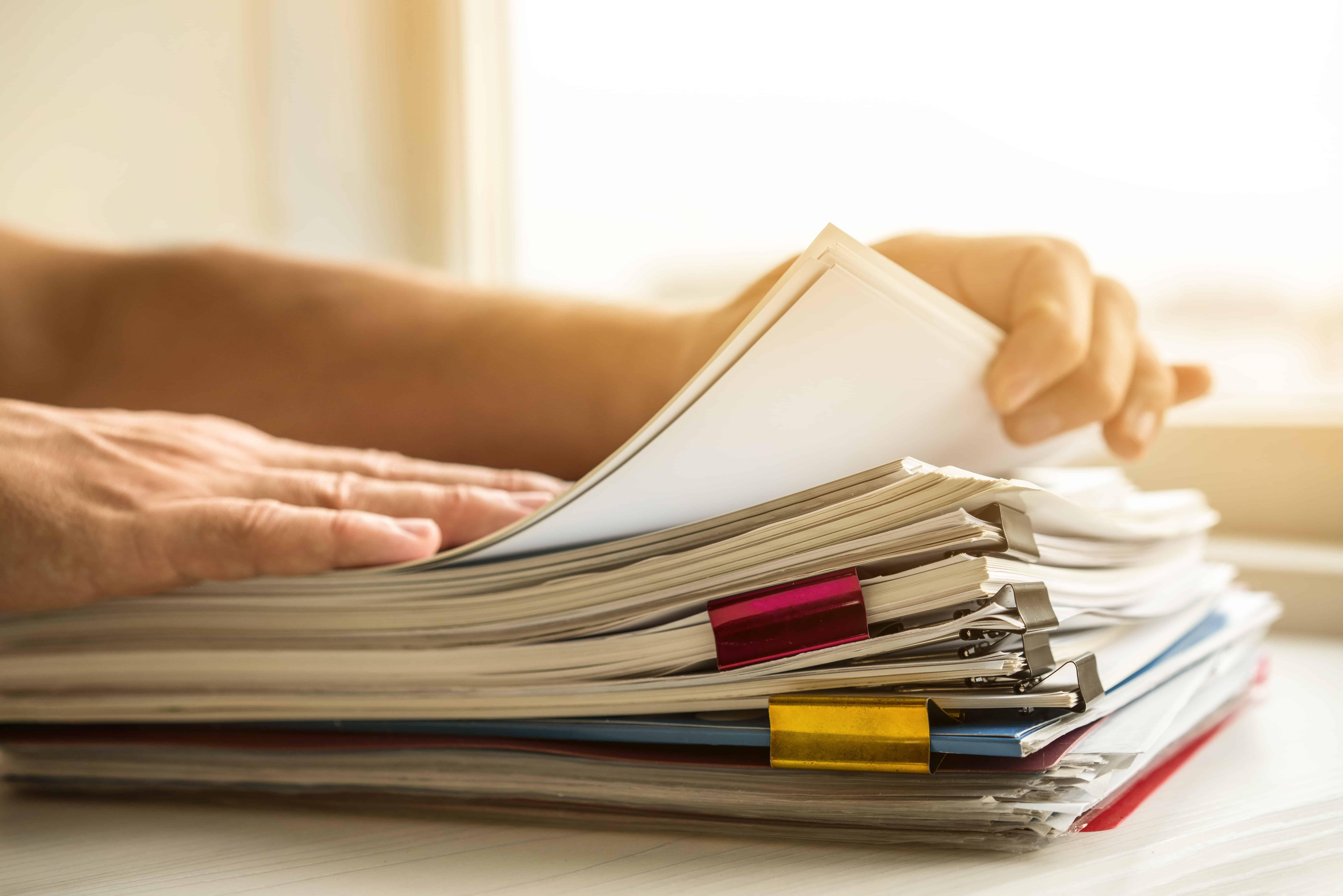 Hands paging through a stack of documents with colored tabs