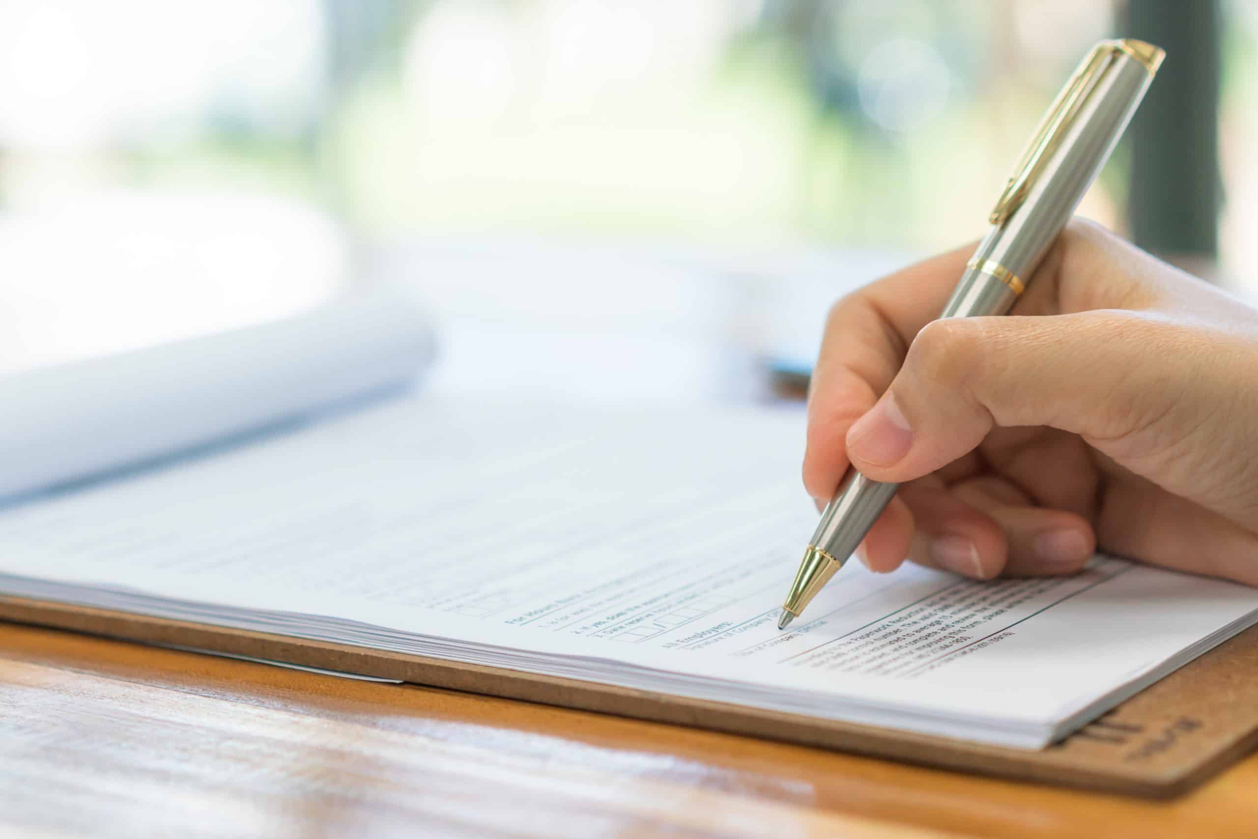 Hand holding a pen signing a document on a wooden desk