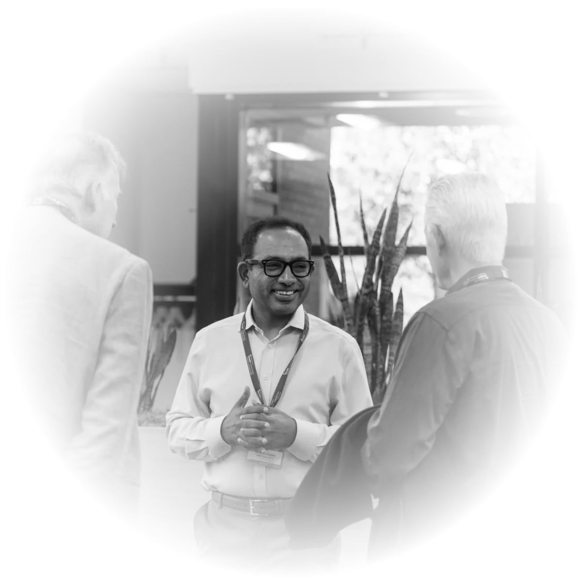 Black-and-white photo of colleagues chatting at an industry event, a smiling man with a lanyard at center