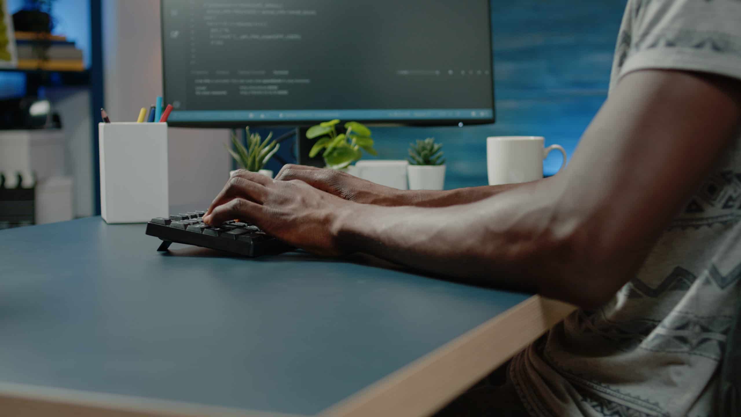 Hands typing on a keyboard in front of a monitor showing code