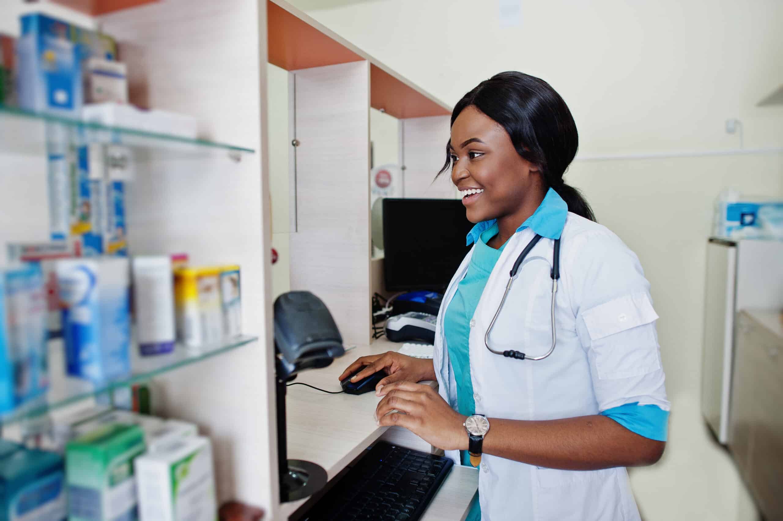 Smiling pharmacist in a white coat using a computer at a pharmacy counter
