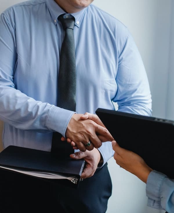 Two business professionals shaking hands, one holding a folder and a tablet