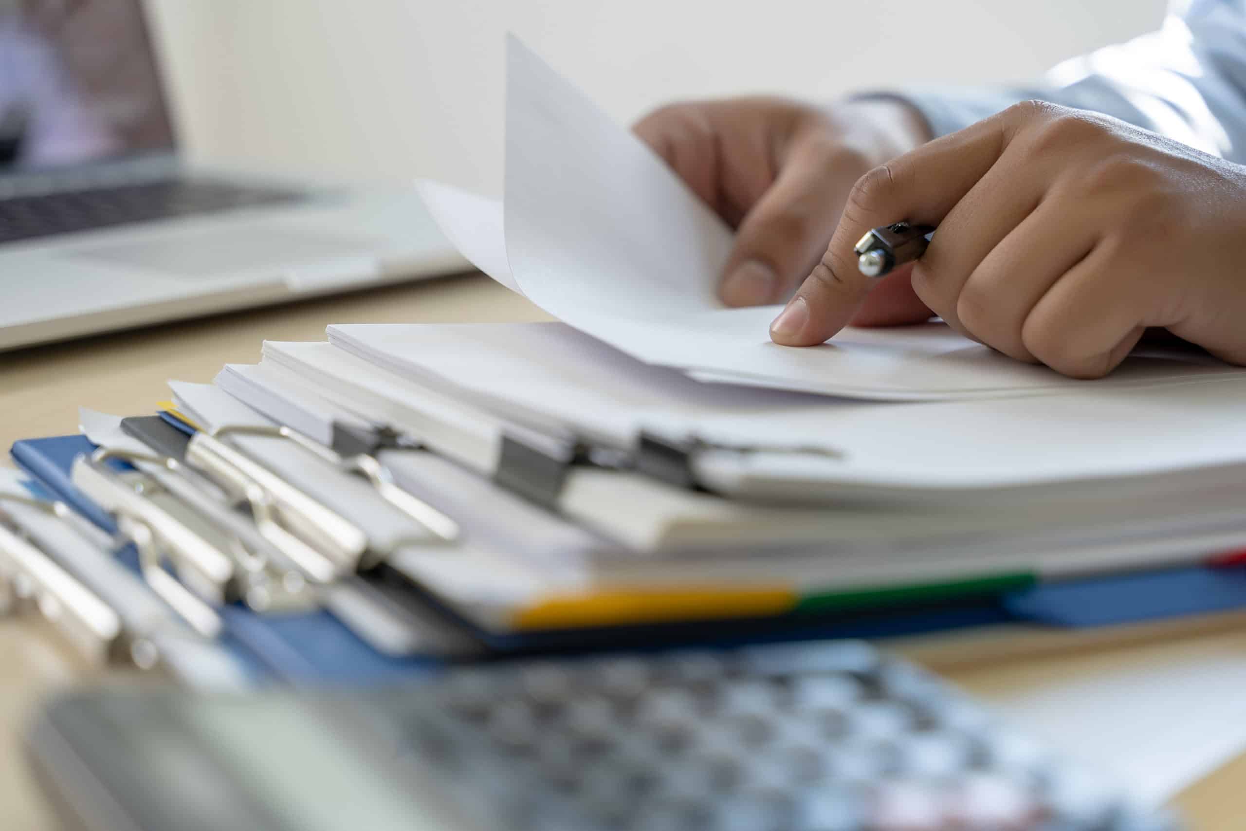 Hand turning pages of a stack of binder-clipped documents