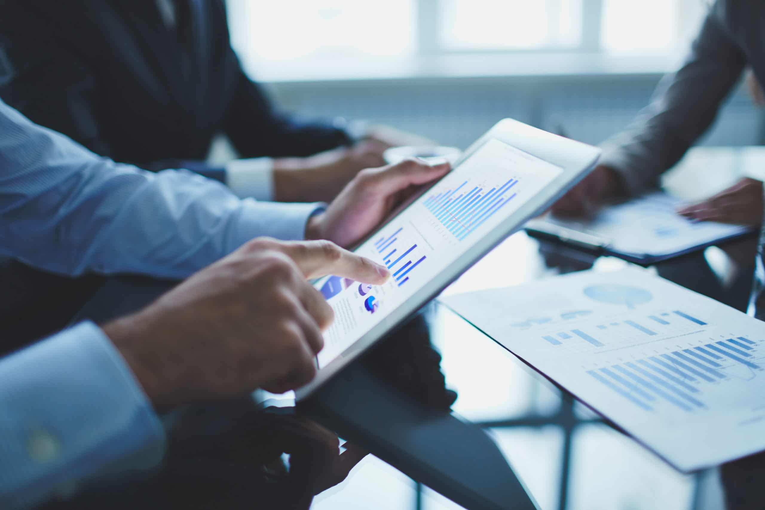 Hand pointing at bar charts on a tablet during a business meeting