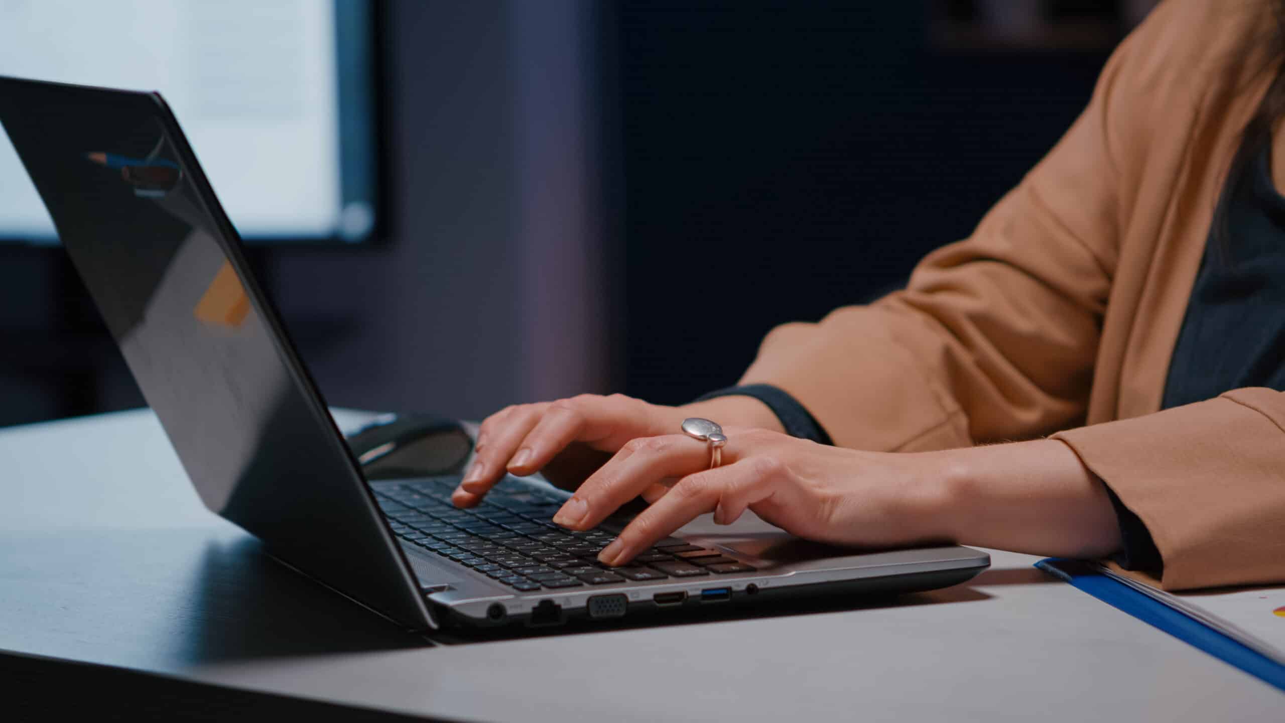 Woman typing on a laptop at a desk in a dim office