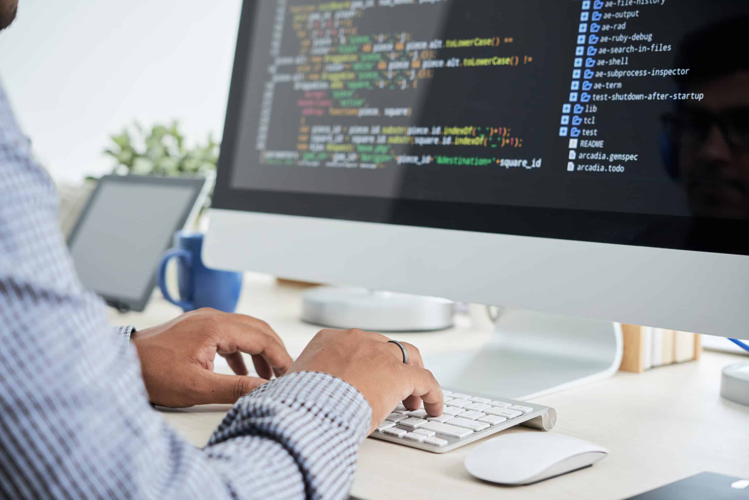 Developer typing at a desktop computer showing lines of code