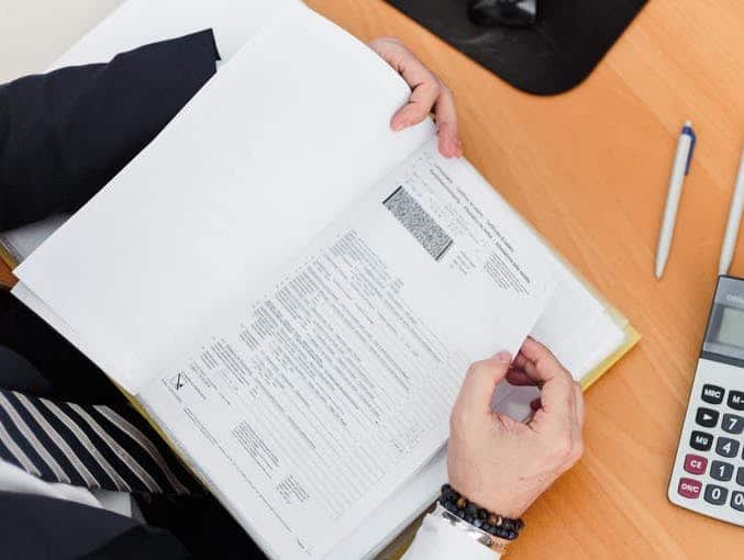 Hands holding a paper form next to a calculator on a wooden desk