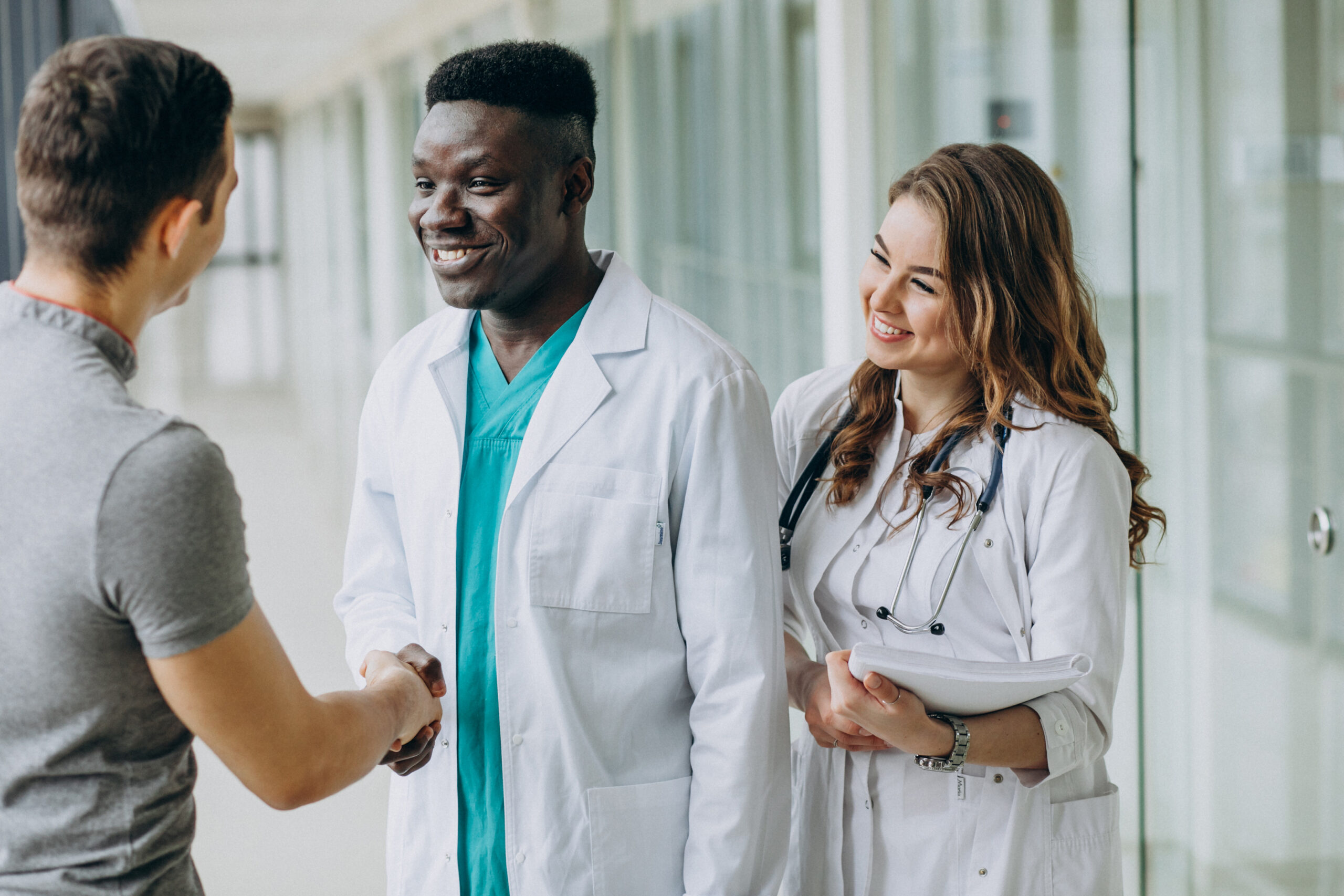 Smiling doctors greeting a patient with a handshake in a hospital corridor