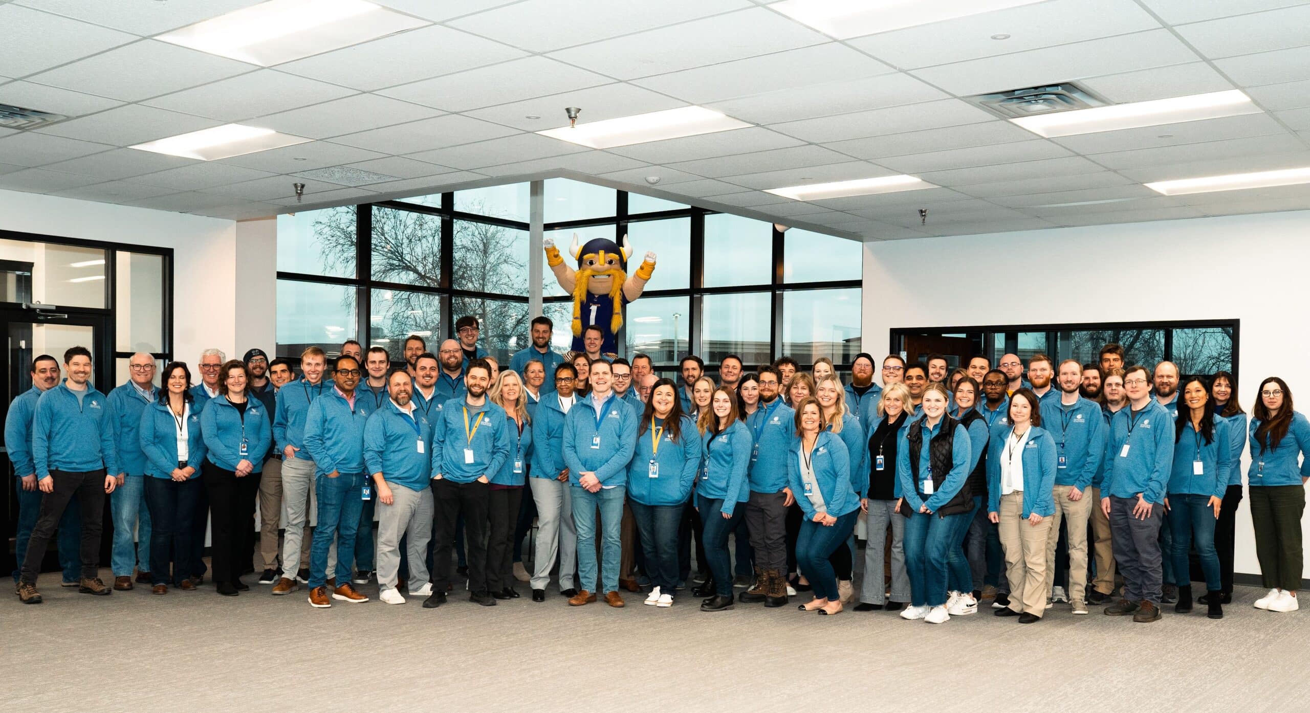 Smart Data Solutions employees in matching blue jackets posing with a Viking mascot at the new headquarters