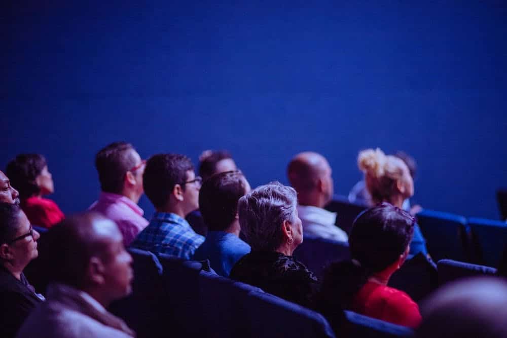 Audience members seated in a dark theater watching a presentation