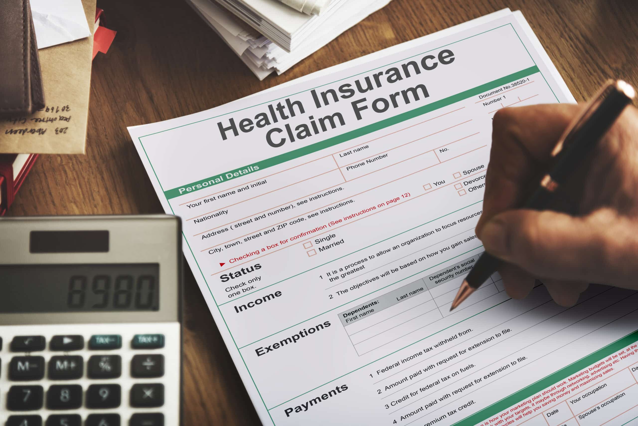 Hand filling out a health insurance claim form next to a calculator