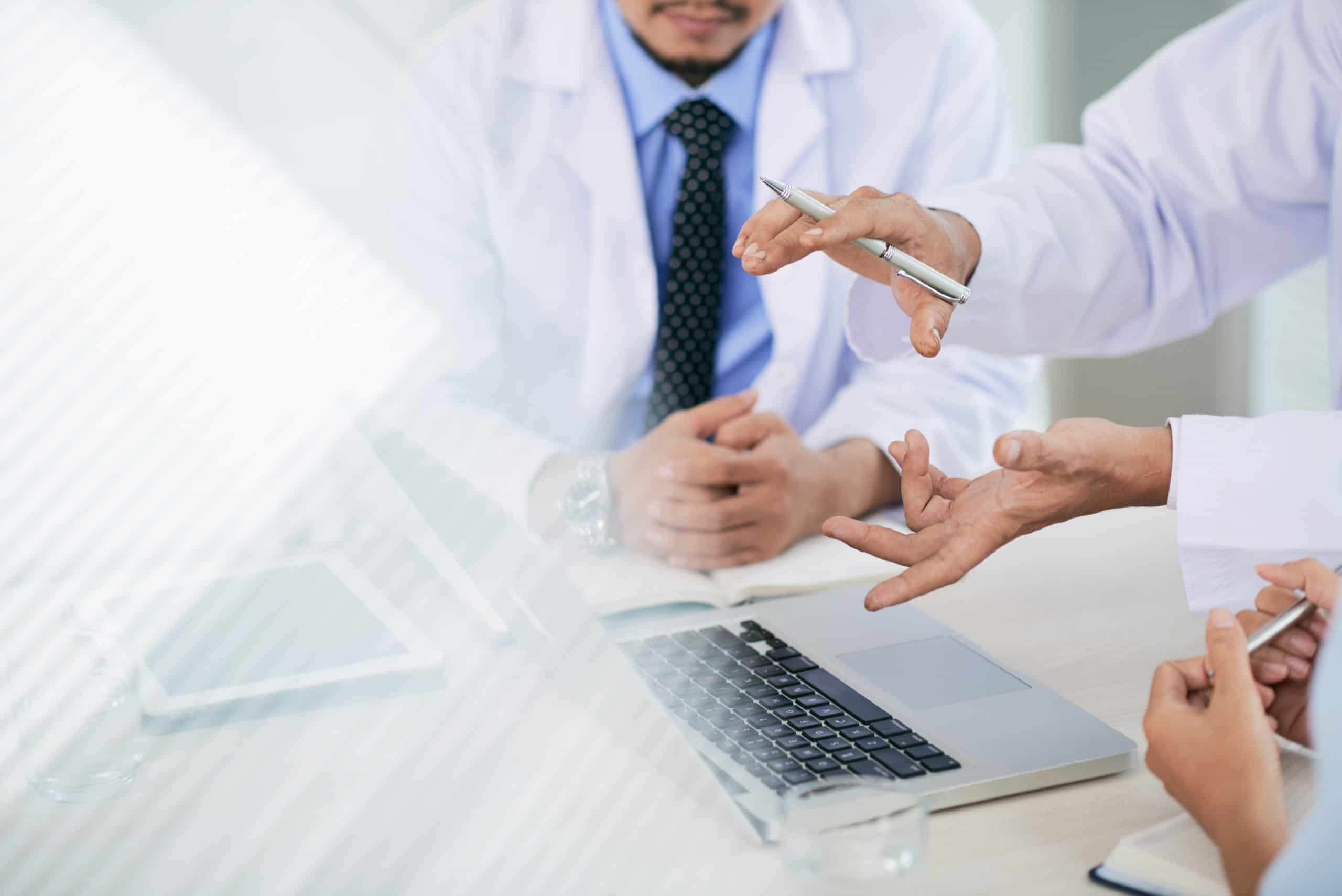 Clinicians in white coats discussing at a table with a laptop and tablet