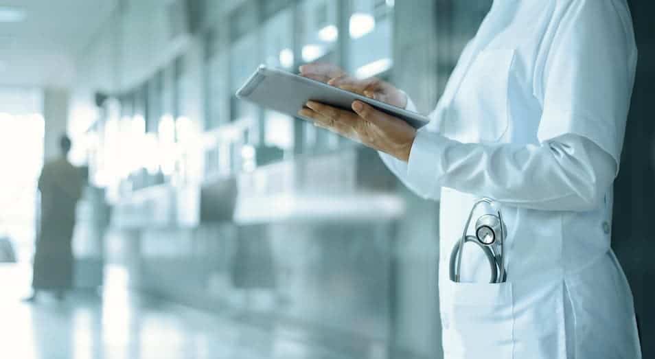 Doctor in a white coat holding a tablet in a blurred hospital corridor