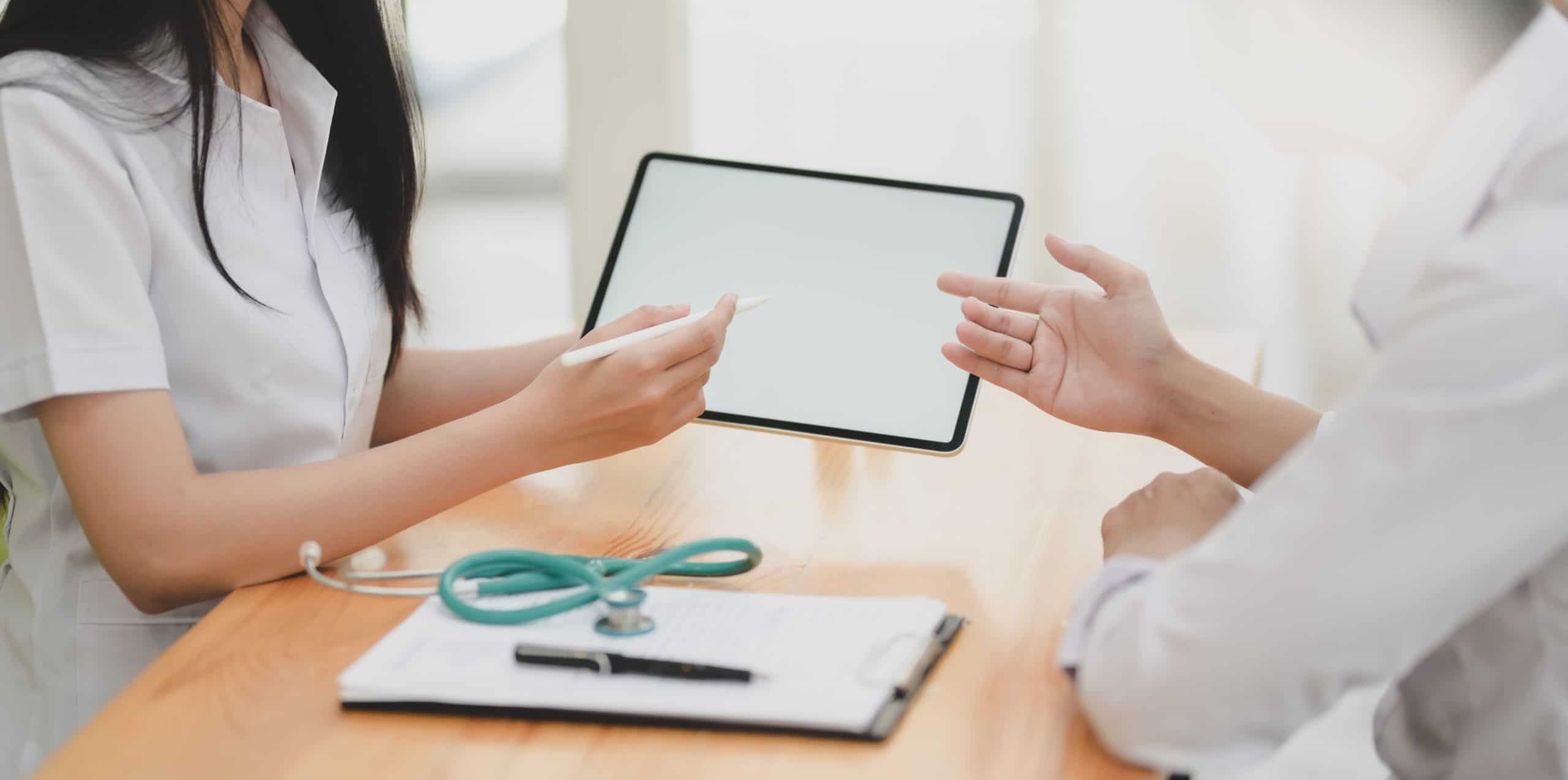 Doctor and patient discussing information on a tablet over a clipboard and stethoscope