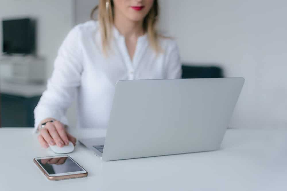 Woman working on a laptop with a smartphone and mouse on a white desk