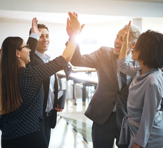 Four colleagues celebrating with a group high five in an office