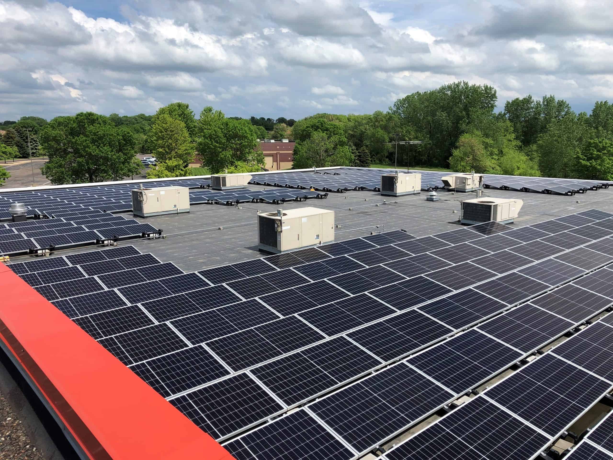 Solar panels installed across a flat commercial rooftop with trees in the background