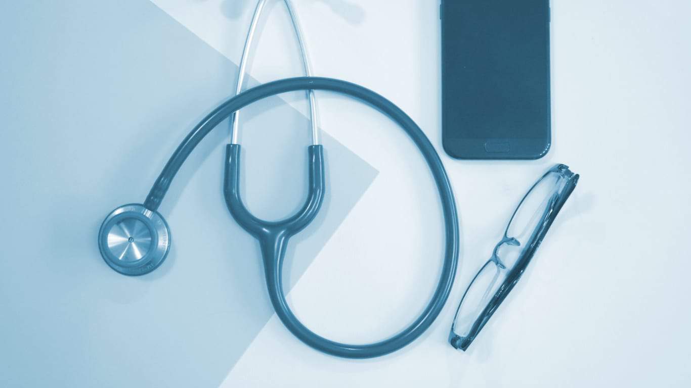 Stethoscope, smartphone and glasses laid out on a desk