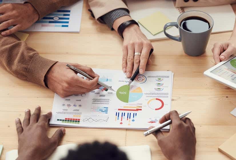 Team members around a table pointing at printed charts and graphs