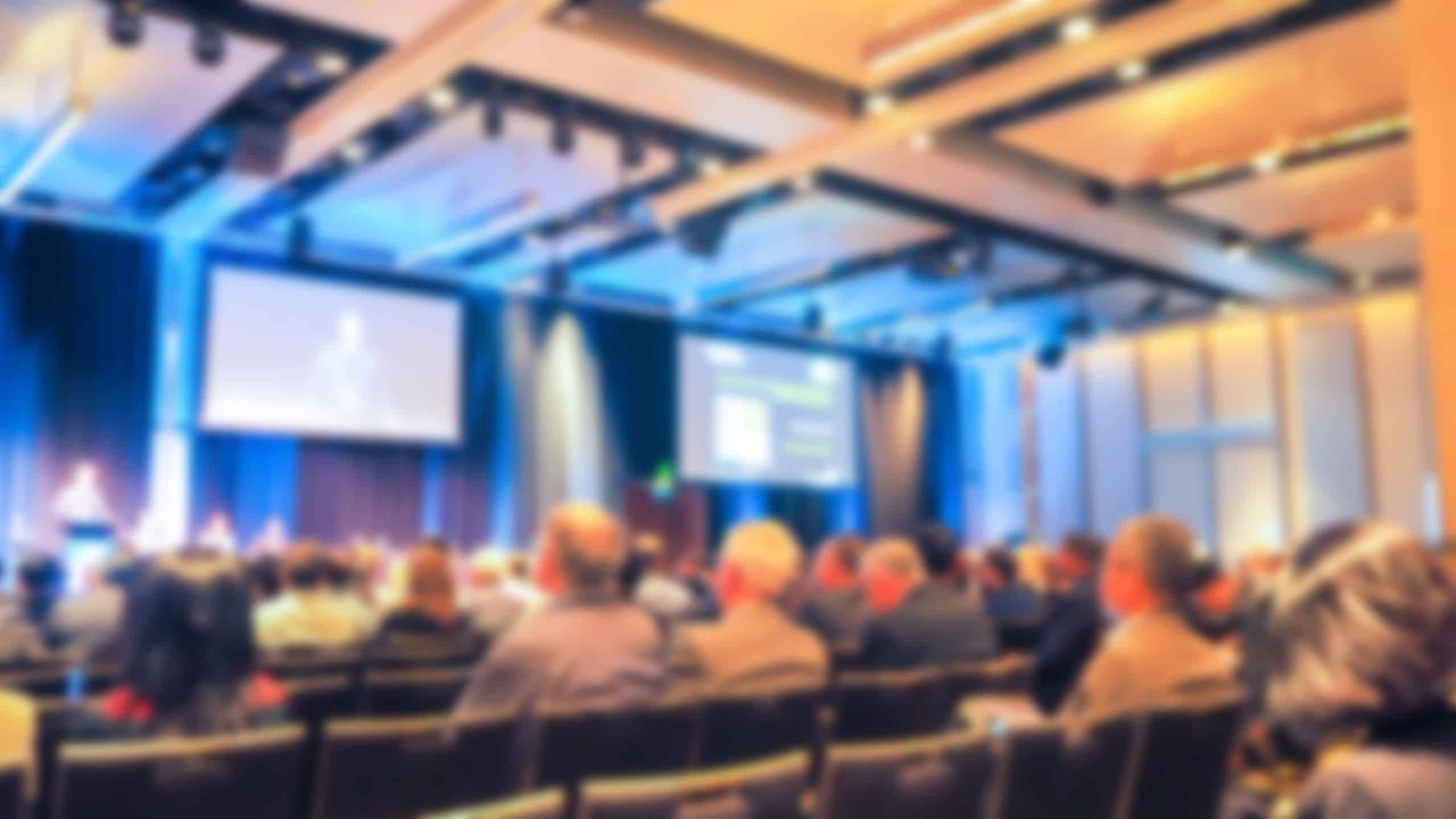 Blurred audience watching a presenter on stage at a conference