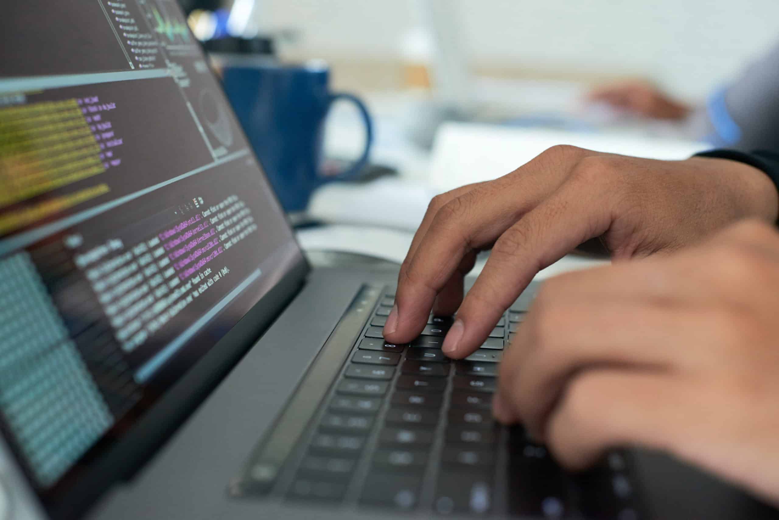Hands typing on a laptop with lines of code on the screen